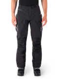 Alpinestars Hyde XT Drystar Pants, calças de aventura e turismo pretas, vestidas por um piloto com botas pretas, com logótipos cinzentos nas coxas, cinto integrado, painéis de joelho reforçados e construção têxtil impermeável