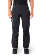 Alpinestars Hyde XT Drystar Pants, calças de aventura e turismo pretas, vestidas por um piloto com botas pretas, com logótipos cinzentos nas coxas, cinto integrado, painéis de joelho reforçados e construção têxtil impermeável