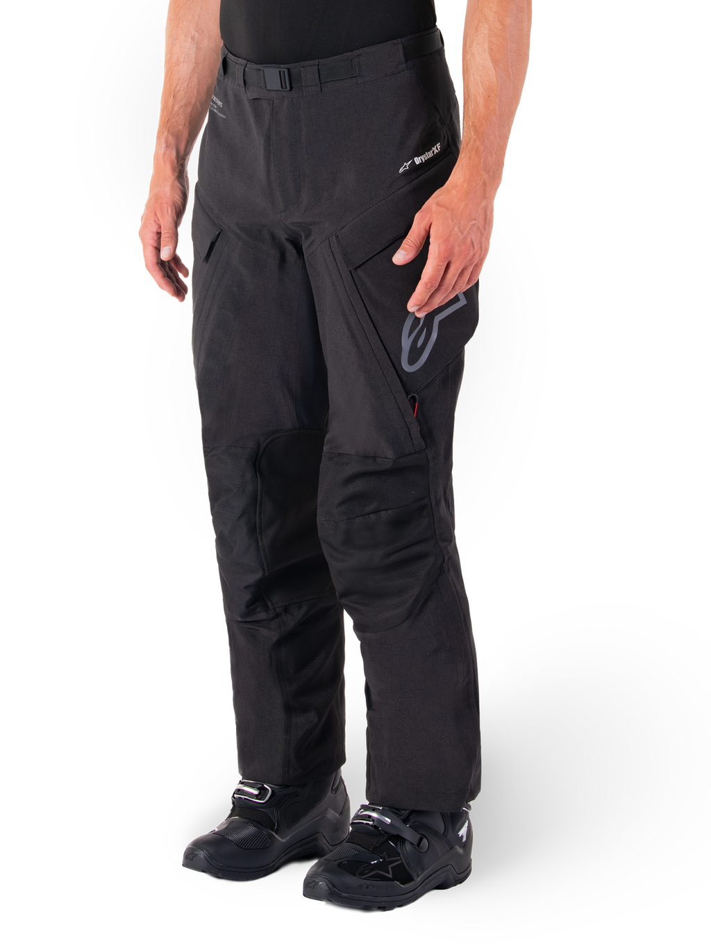 Calças Alpinestars Hyde XT Drystar®, calças de motociclismo Adventure Touring, pretas, usadas com botas pretas, apresentando o logótipo da membrana laminada Drystar®XF, painéis reforçados nos joelhos e bolsos de carga com fecho de correr.