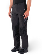 Calças Alpinestars Hyde XT Drystar®, calças de motociclismo Adventure Touring, pretas, usadas com botas pretas, apresentando o logótipo da membrana laminada Drystar®XF, painéis reforçados nos joelhos e bolsos de carga com fecho de correr.