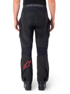 Calças Alpinestars Hyde XT Drystar®, calças de motociclismo de aventura, pretas com logótipo de estrela vermelho na parte inferior da perna, vista traseira, design enduro para usar por cima da bota, painéis têxteis duráveis e cintura com a marca