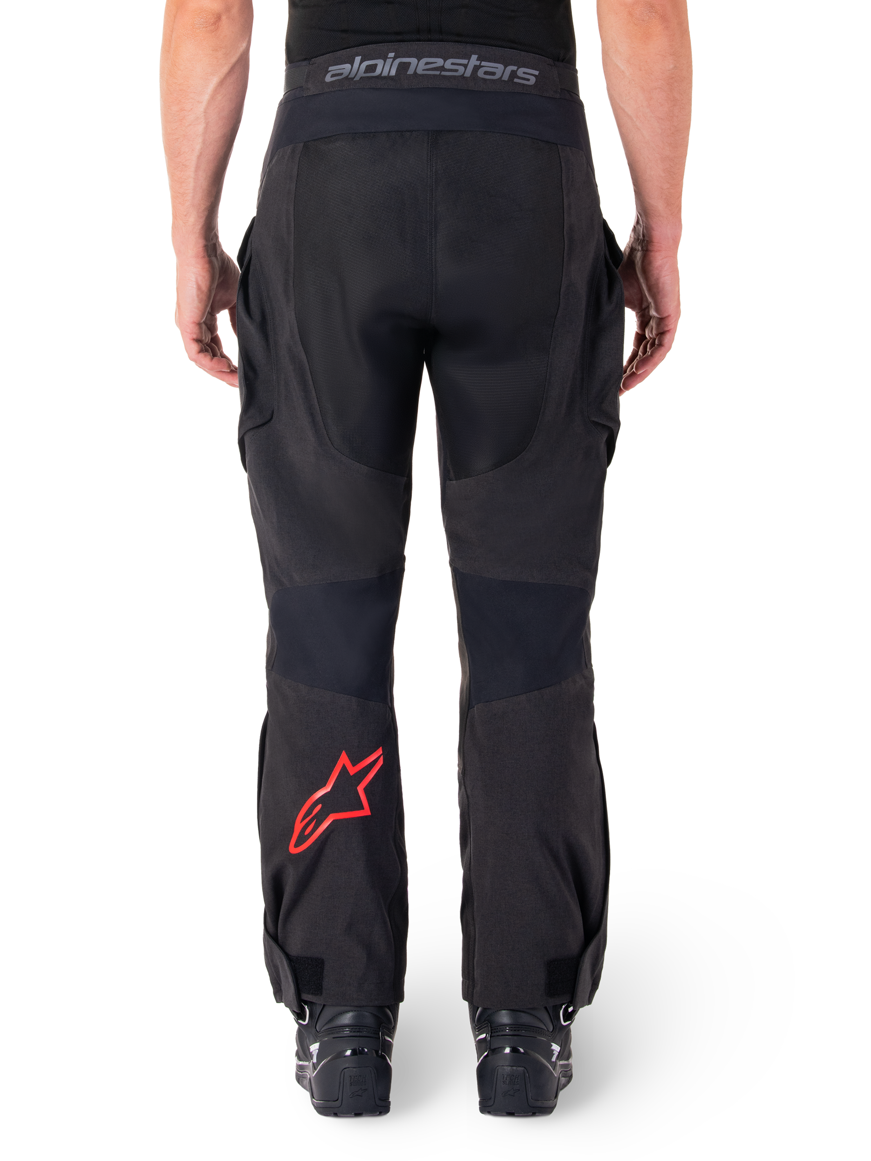 Calças Alpinestars Hyde XT Drystar®, calças de motociclismo de aventura, pretas com logótipo de estrela vermelho na parte inferior da perna, vista traseira, design enduro para usar por cima da bota, painéis têxteis duráveis e cintura com a marca