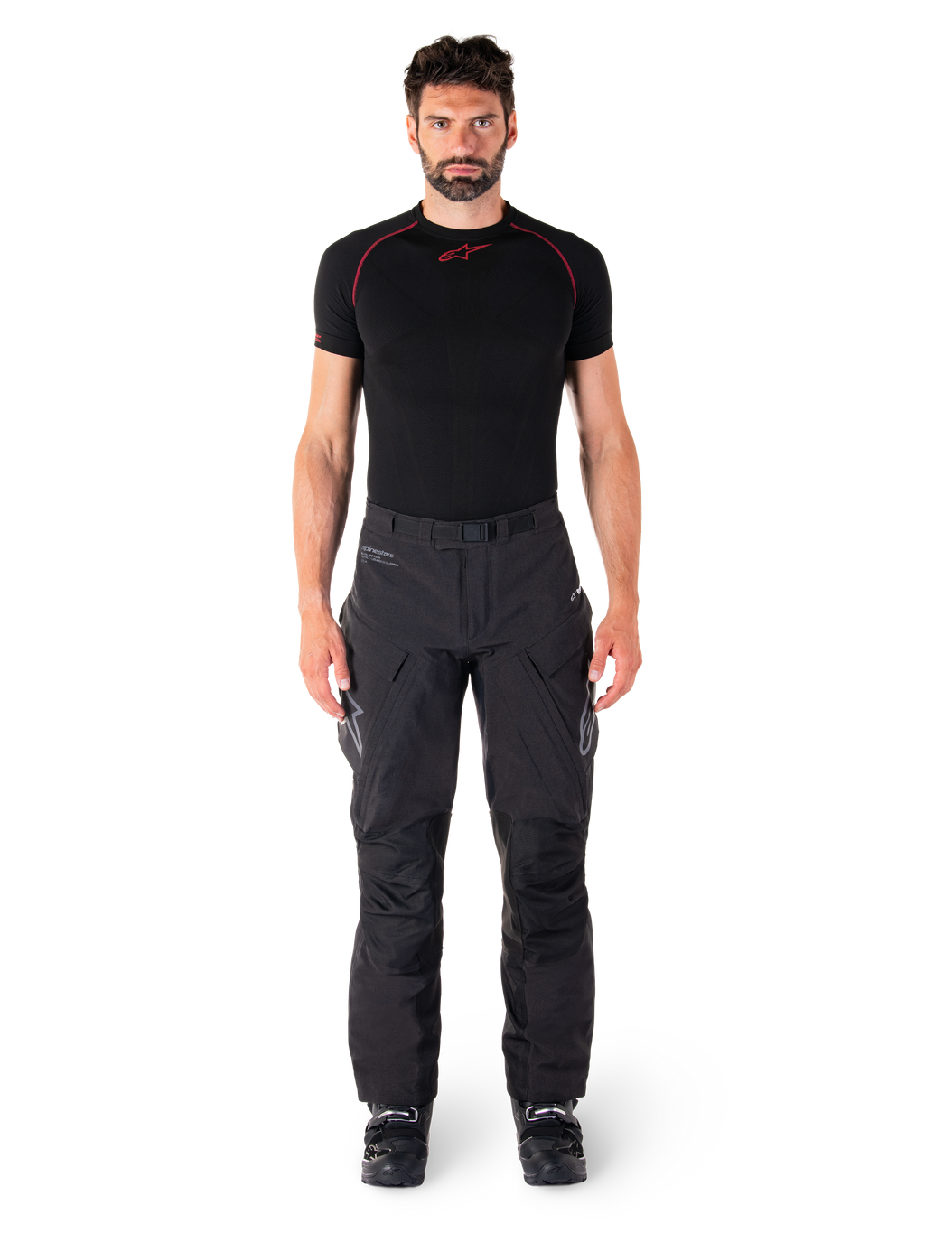 Calças Alpinestars Hyde XT Drystar®, calças de motociclismo Adventure Touring, pretas, vestidas por um modelo com uma camisola interior de manga curta preta e botas pretas, com material elástico técnico, painéis reforçados nos joelhos e bolsos de carga ergonómicos.