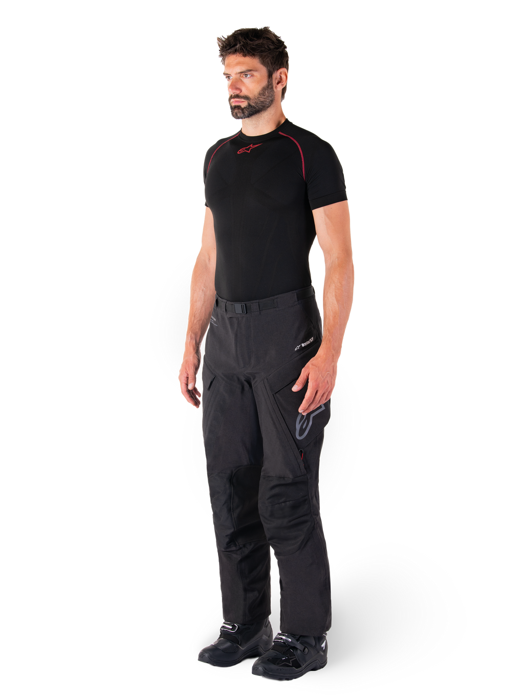 Calças Alpinestars Hyde XT Drystar®, calças pretas de motociclismo adventure touring vestidas por um modelo com uma camisola de compressão preta e botas pretas, com construção técnica impermeável e logótipo Drystar®XF.