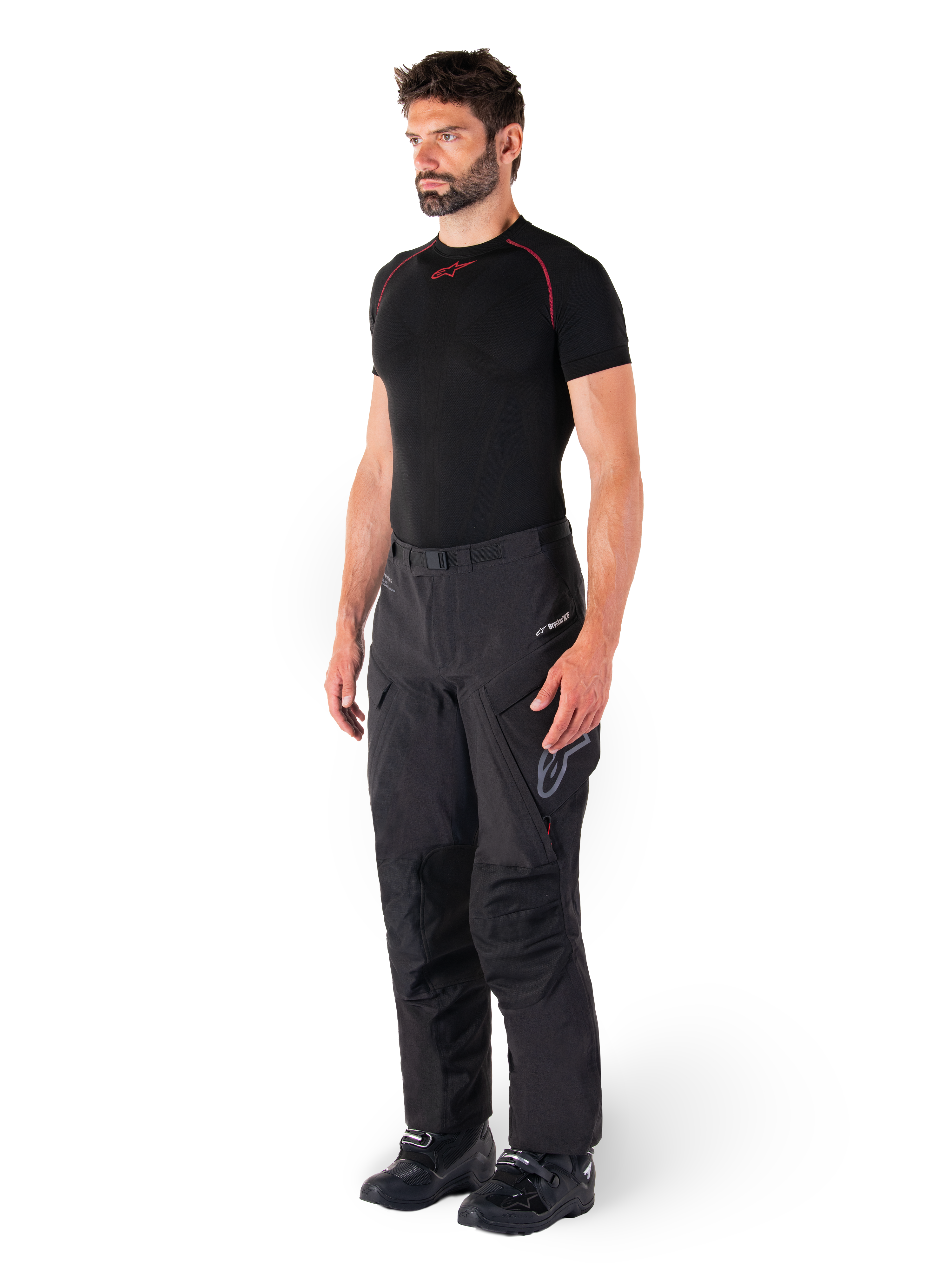 Calças Alpinestars Hyde XT Drystar®, calças pretas de motociclismo adventure touring vestidas por um modelo com uma camisola de compressão preta e botas pretas, com construção técnica impermeável e logótipo Drystar®XF.