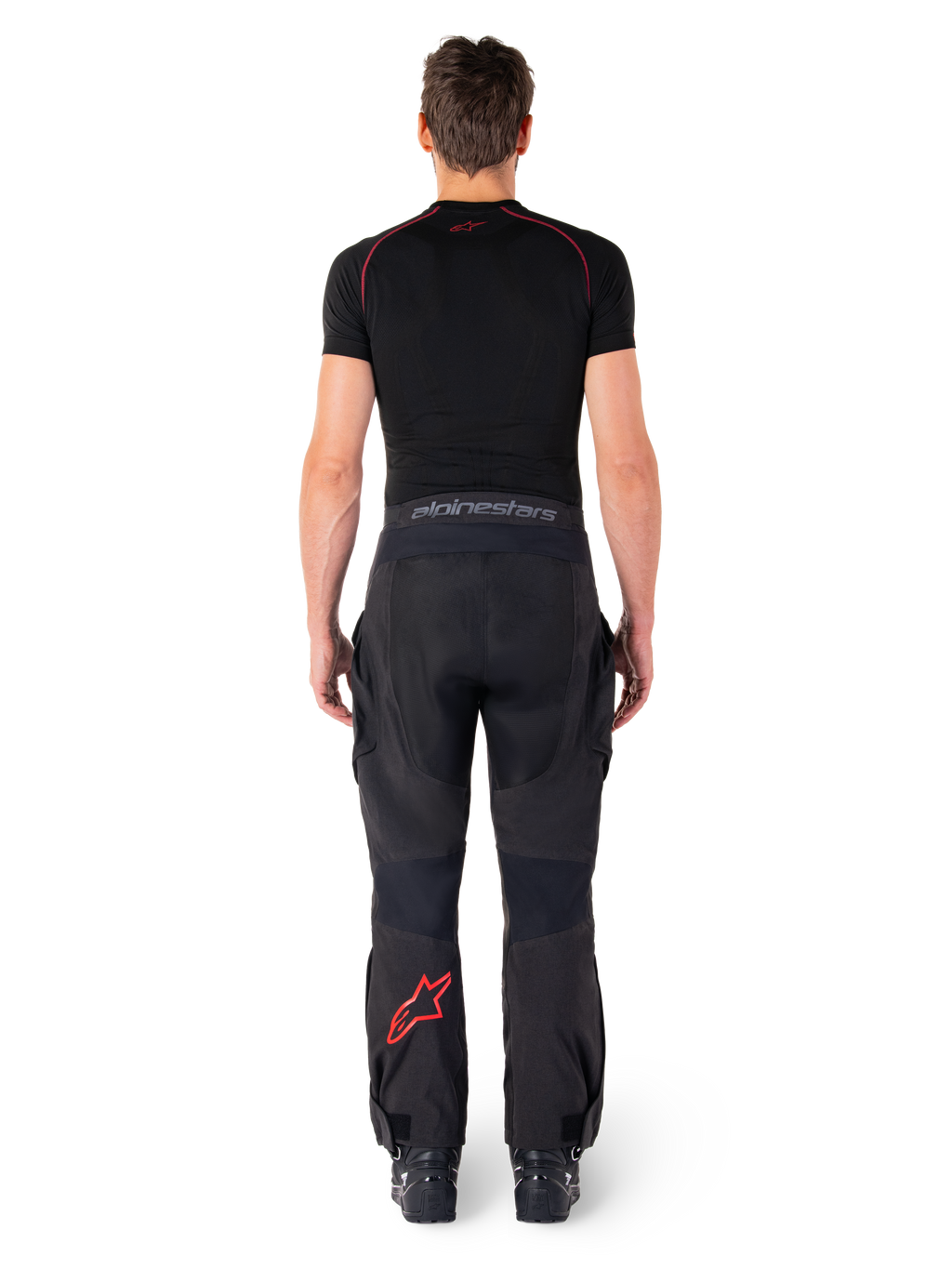 Alpinestars Hyde Xt Drystar® Pants, calças de motociclismo Adventure Touring, pretas e vermelho vivo, vista traseira de um piloto a usar as calças e uma camada de base preta, com logótipo de estrela vermelha na perna esquerda e marca cinzenta no cós