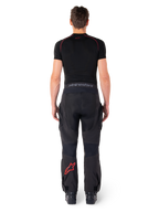 Alpinestars Hyde Xt Drystar® Pants, calças de motociclismo Adventure Touring, pretas e vermelho vivo, vista traseira de um piloto a usar as calças e uma camada de base preta, com logótipo de estrela vermelha na perna esquerda e marca cinzenta no cós