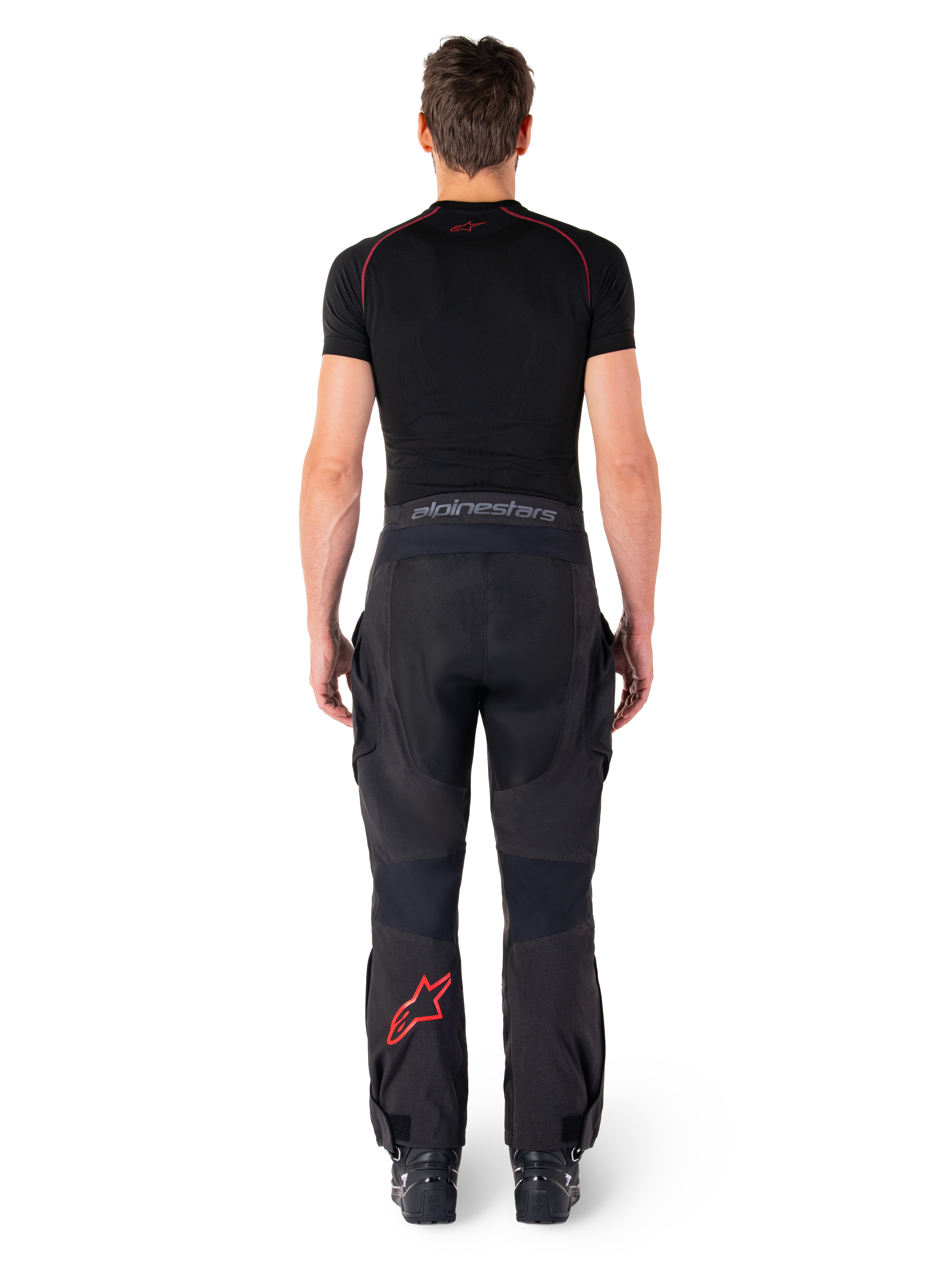 Alpinestars Hyde Xt Drystar® Pants, calças de motociclismo Adventure Touring, pretas e vermelho vivo, vista traseira de um piloto a usar as calças e uma camada de base preta, com logótipo de estrela vermelha na perna esquerda e marca cinzenta no cós