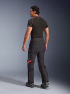 Calças Laminadas Alpinestars Halo Pro Drystar® XF, cor Black Dark Shadow com detalhes em vermelho, vista traseira num modelo masculino, combinadas com uma camada de base preta e botas de motociclismo, equipamento técnico de aventura para todo o terreno