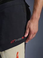 Alpinestars Halo Pro Drystar® XF Laminated Pants, calças de motociclismo de aventura em Mastic Black, primeiro plano da lateral da coxa mostrando o logótipo Drystar XF Extra Flow a vermelho e branco, construção têxtil com painéis de cores mistas