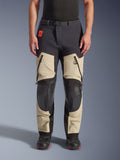 Alpinestars Halo Pro Drystar® XF Laminated Pants, calças de motociclismo de aventura, Mastic Black, vista frontal usada por um piloto, com grandes aberturas com fecho nas coxas, painéis reforçados pretos nos joelhos e construção em têxtil bege, combinadas com botas de motociclismo pretas e vermelhas