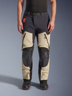 Alpinestars Halo Pro Drystar® XF Laminated Pants, calças de motociclismo de aventura, Mastic Black, vista frontal usada por um piloto, com grandes aberturas com fecho nas coxas, painéis reforçados pretos nos joelhos e construção em têxtil bege, combinadas com botas de motociclismo pretas e vermelhas