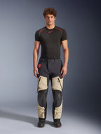 Alpinestars Halo Pro Drystar® XF Laminated Pants, Mastic Black, calças de motociclismo de aventura vestidas por um modelo com uma camada base preta e botas, apresentando painéis bege nas coxas com grandes aberturas de ventilação com fecho, secções reforçadas nos joelhos a preto e um cinto com fivela magnética.