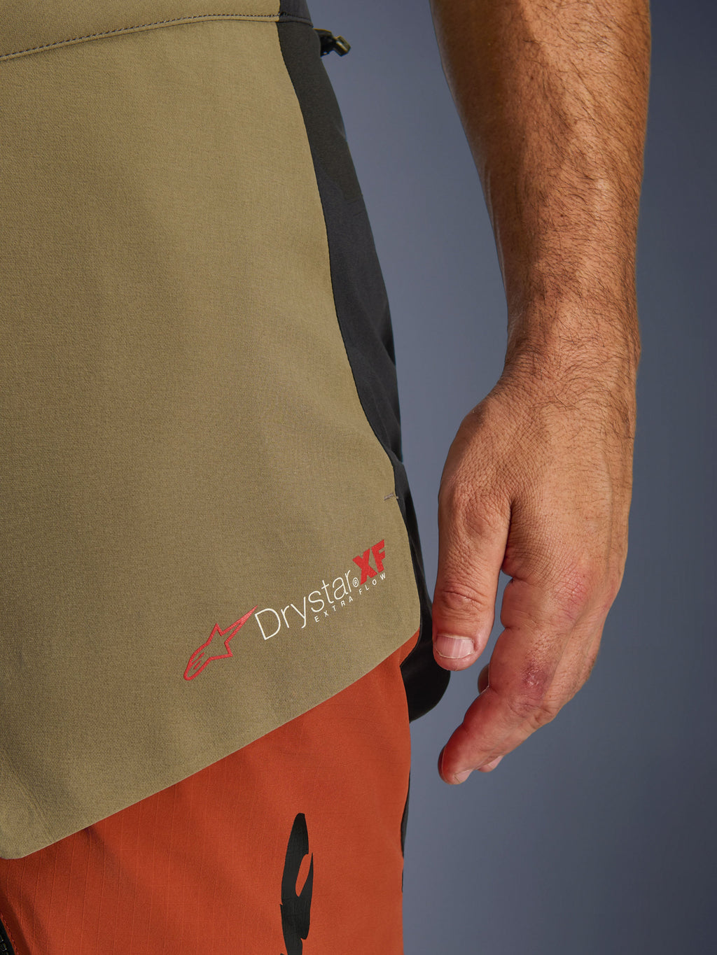 Calças Alpinestars Halo Pro Drystar® XF Laminated, Walnut Rust Black, detalhe em grande plano da marca Drystar XF Extra Flow, mostrando os painéis têxteis em verde azeitona e laranja ferrugem e a construção técnica.