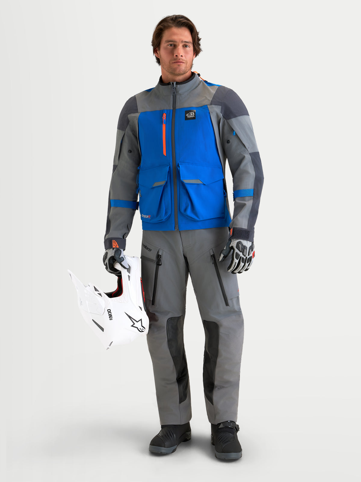 Maxdura Drystar Xf Laminated Calças da Alpinestars, calças de moto adventure para homem em cinzento e preto, num modelo a segurar um capacete off-road branco