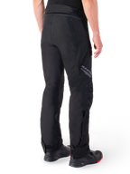 Alpinestars St-1 Waterproof Pants, Black, rear view showing textile construction and Alpinestars branding on the thigh, worn with black motorcycle boots, adventure touring style