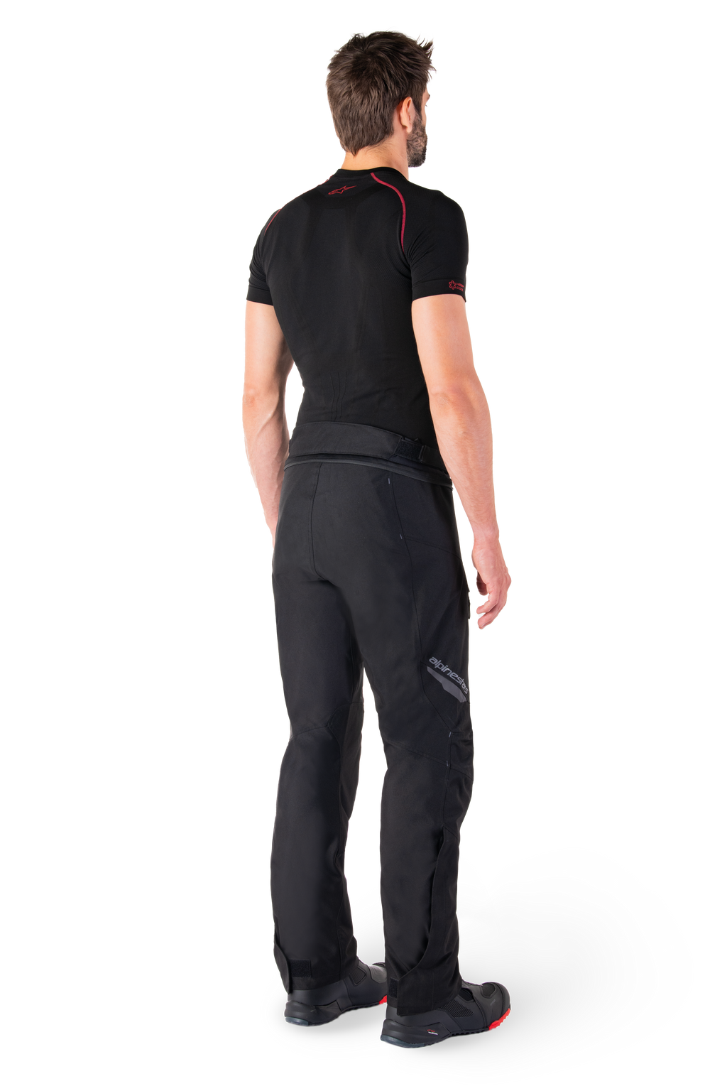 Alpinestars St-1 Waterproof Pants, Black motorcycle touring pants, three-quarter rear view on a model wearing a black base layer and black riding boots, featuring reflective Alpinestars branding on the thigh and a streamlined ergonomic design.