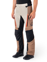 Alpinestars ST-1 Waterproof Pants, Adventure Touring Pants, Dark Khaki Sand Black and Red Fluo, featuring zippered front pockets and black reinforced panels on the knees and inner legs, worn with black riding shoes, ergonomic textile design for all-weather riding