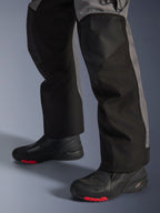 Calças Alpinestars Andes V4 Drystar®, calças têxteis de motociclismo, pretas e cinzento escuro, usadas com botas de motociclismo pretas com solas vermelhas, design adventure touring com painéis de perna reforçados e corte reto.
