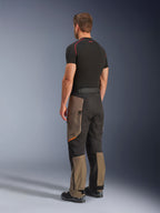 Calças Alpinestars Cusco Drystar®, calças de motociclismo de aventura, Walnut Black, vista traseira de três quartos, usadas com uma camada base preta e botas, com painéis têxteis reforçados, bolsos cargo com fecho nas coxas e um corte touring ergonómico.