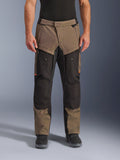 Calças Alpinestars Cusco Drystar®, calças de motociclismo adventure touring, walnut e preto com pormenores cor de laranja, vista frontal num modelo, construção em tecido técnico, bolsos cargo e fechos de ventilação, usadas com botas de motociclismo pretas