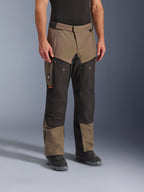 Calças Alpinestars Cusco Drystar®, calças de motociclismo de aventura, Walnut Black, apresentadas num modelo com botas pretas, com um design multi-painel em castanho e preto, bolsos com fecho e joelhos reforçados para turismo