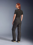Calças Alpinestars Stella Andes V4 Drystar®, pretas, calças de motociclismo de aventura vistas de um ângulo lateral traseiro numa modelo, combinadas com uma t-shirt preta e botas, com bolsos cargo laterais, logótipo branco e construção têxtil durável.