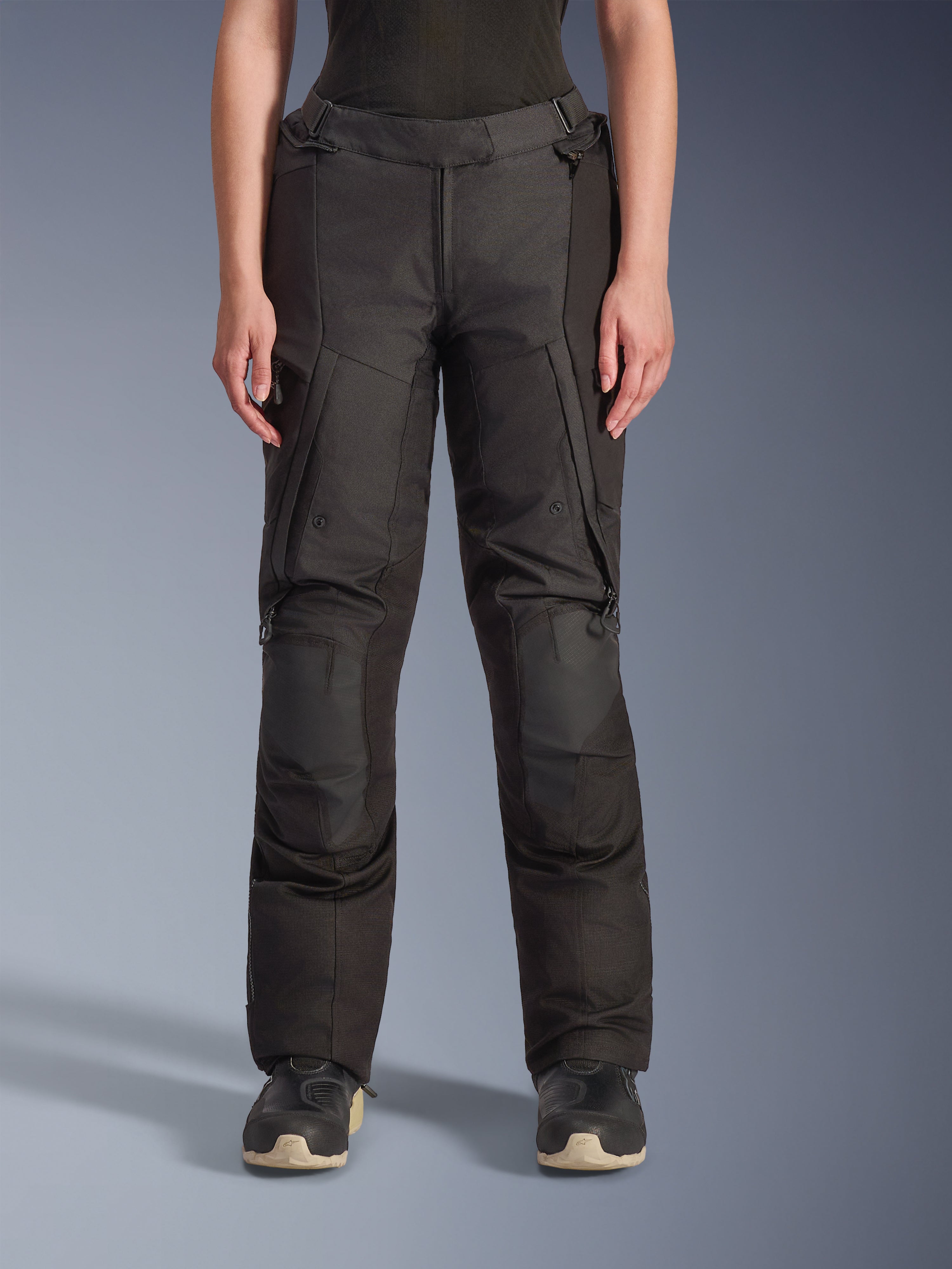 Alpinestars Stella Andes V4 Drystar Pants, calças de aventura para mulher, pretas, vista frontal, com painéis reforçados nos joelhos, bolsos cargo resistentes à água e correias de ajuste na cintura, usadas com botas pretas em cenário de estúdio