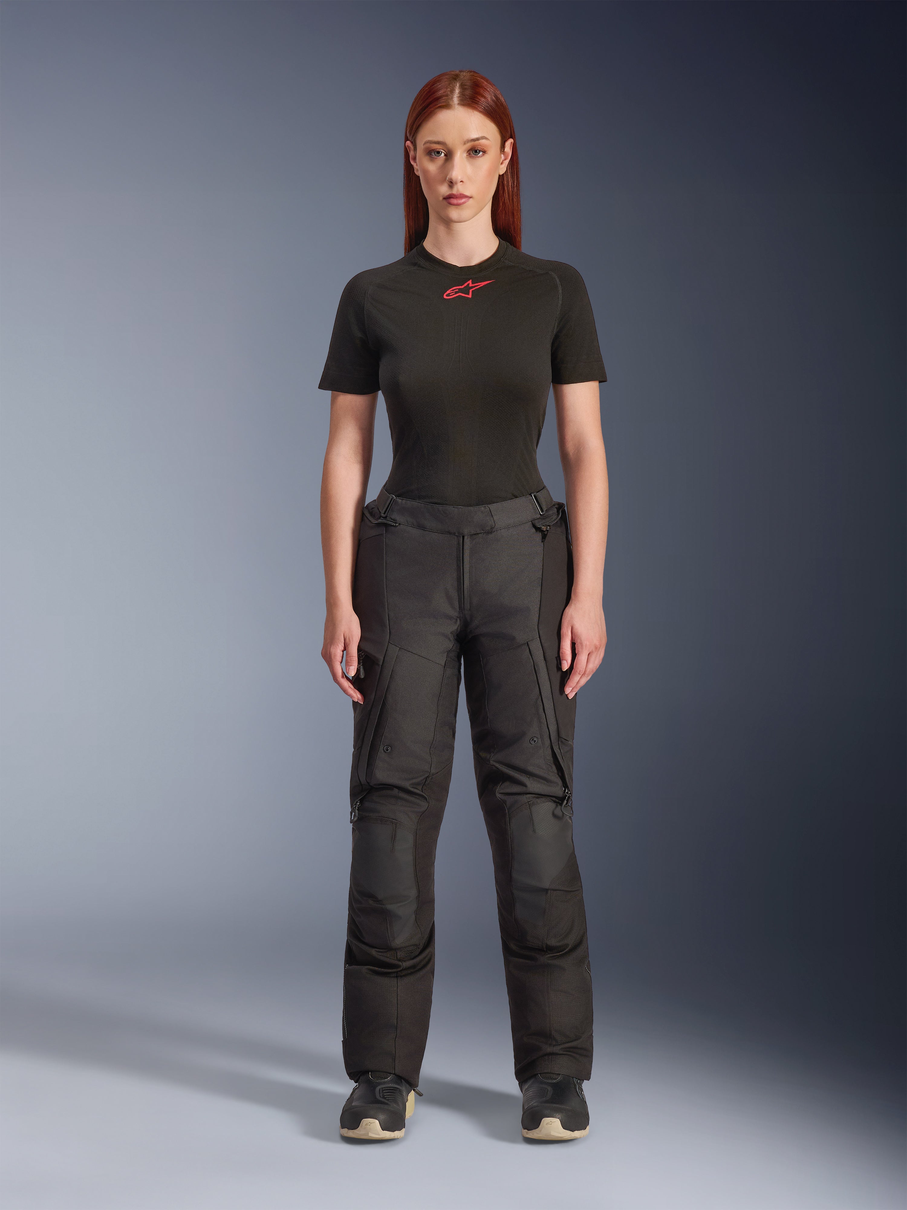 Calças Alpinestars Stella Andes V4 Drystar®, calças de motociclismo de aventura e touring para mulher, pretas, apresentadas numa modelo com uma t-shirt Alpinestars preta, com um design têxtil técnico, bolsos cargo e painéis reforçados nos joelhos.