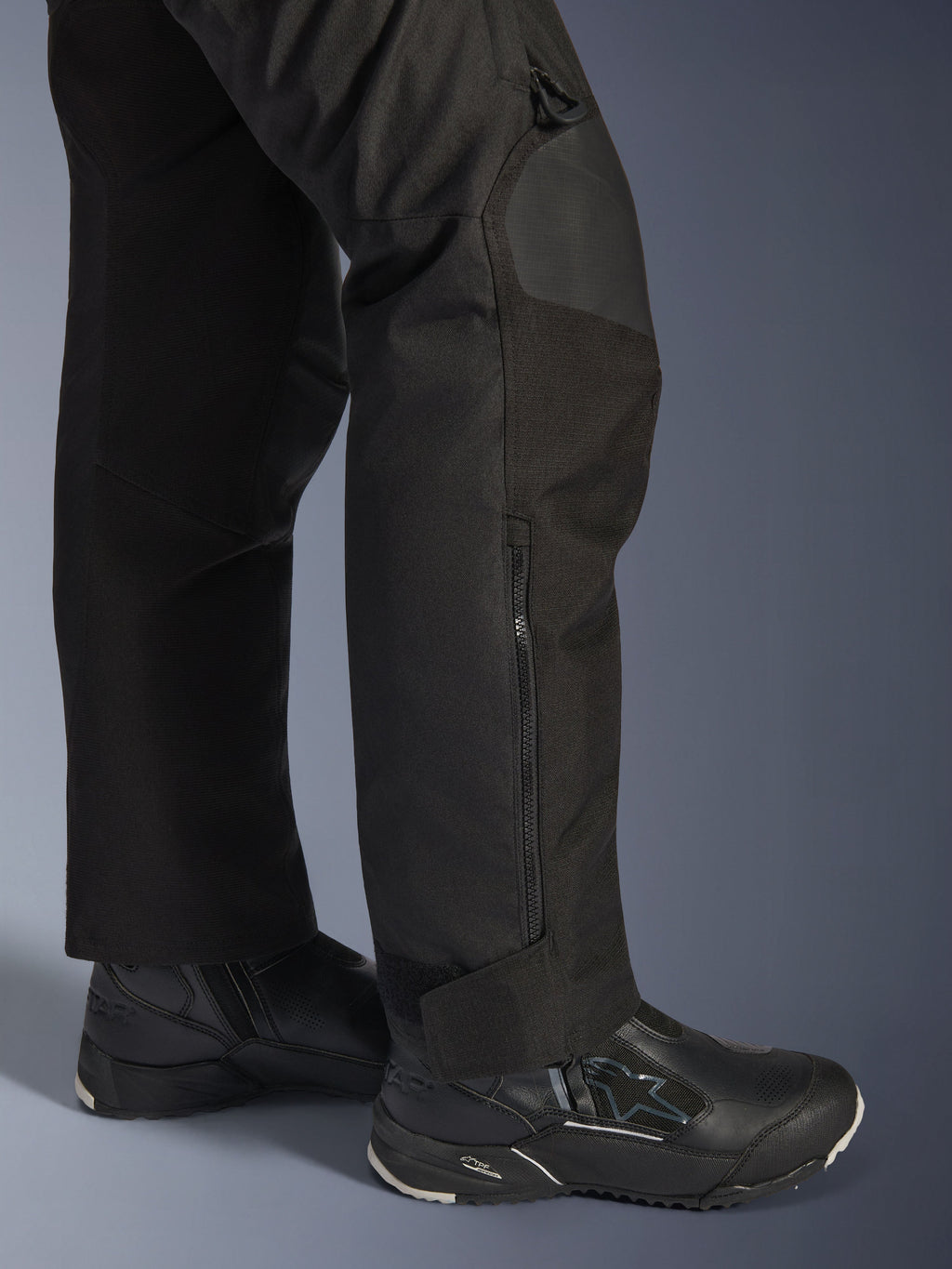 Calças Alpinestars Stella Andes V4 Drystar®, calças de motociclismo para mulher, pretas, grande plano da zona inferior da perna com fecho lateral e ajuste no tornozelo, usadas com botas de motociclismo Alpinestars pretas