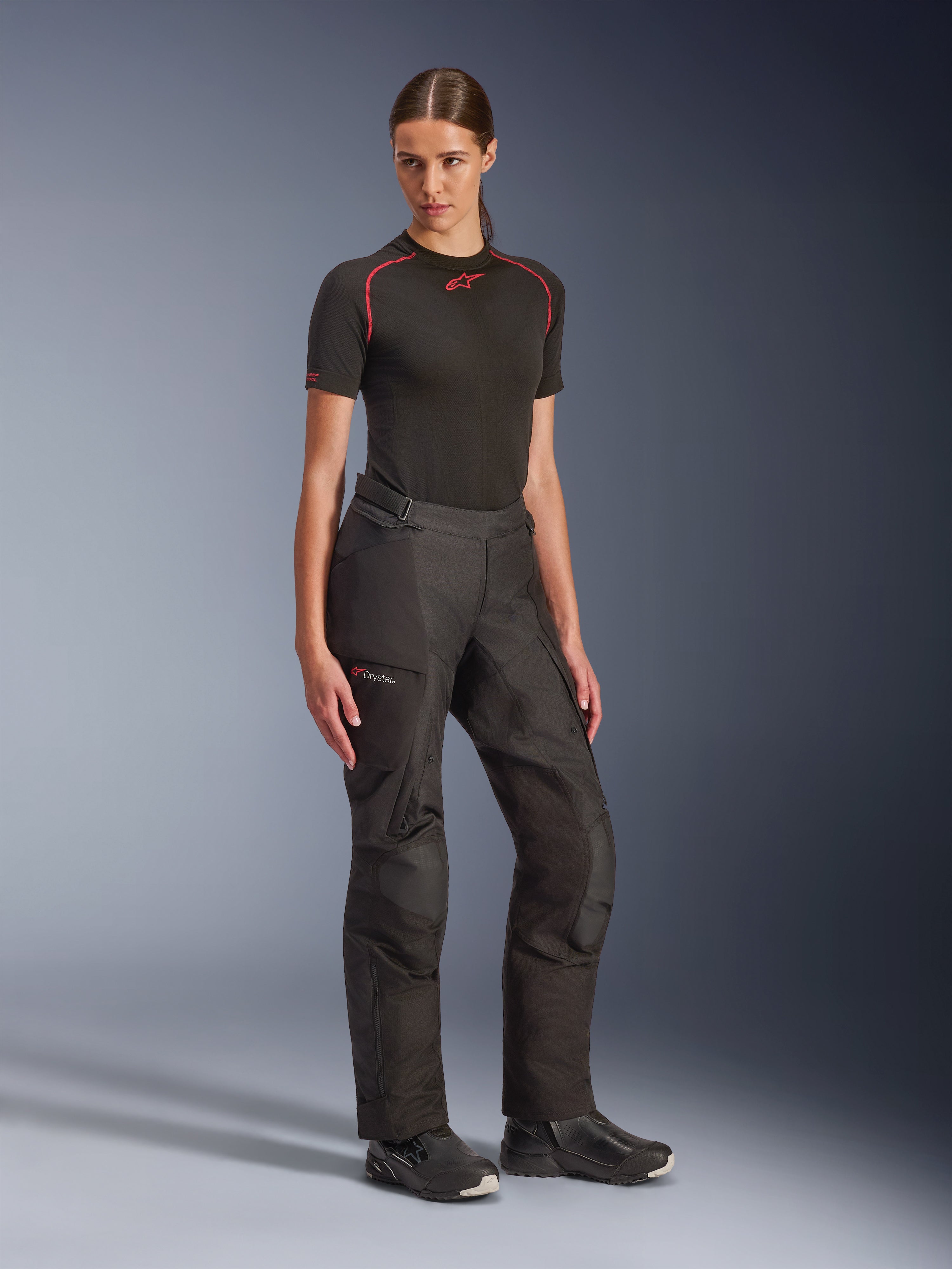 Calças Alpinestars Stella Andes V4 Drystar®, pretas, calças de motociclismo de aventura para mulher, usadas com uma camisola técnica de manga curta preta e botas de motociclismo pretas, com tecnologia Drystar® impermeável e bolsos cargo