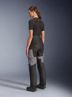 Calças Alpinestars Stella Andes V4 Drystar® para Mulher, calças de motociclismo adventure-touring pretas e cinzento escuro, vista lateral e traseira numa modelo, com construção têxtil durável, painéis de reforço cinzentos e ajuste ergonómico feminino.