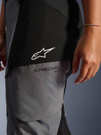 Calças Femininas Stella Andes V4 Drystar®, Preto e Cinzento Escuro, grande plano da parte superior da coxa com logótipo de estrela branca e marca Alpinestars a preto, material têxtil durável para touring de aventura