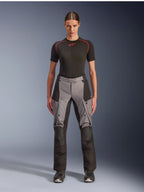 Calças Alpinestars Stella Andes V4 Drystar, calças de motociclismo touring de aventura para mulher, pretas e cinzento escuro, vestidas por uma modelo com uma camada base preta e botas de motociclista, apresentando painéis têxteis reforçados e bolsos cargo para condução de aventura