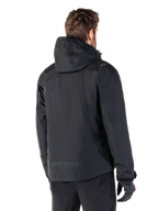 Alpinestars Morush Waterproof Parka, Black, rear view of a man wearing the hooded motorcycle jacket, featuring raglan sleeves, an extended rear hem for coverage, MO.ST.EQ. branding on the lower back, and a subtle Alpinestars logo on the shoulder, urban streetwear style