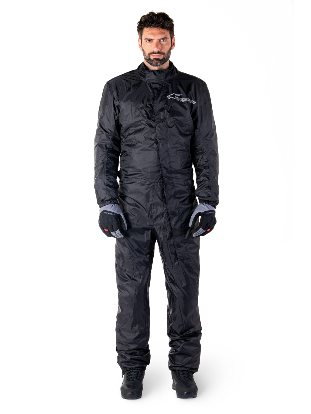 Alpinestars Hurricane Rain V2 Suit, Full-Body Motorcycle Rain Suit in Black, waterproof protective gear with high collar and front storm closure, featuring white logo on chest, worn with black and grey gloves and boots