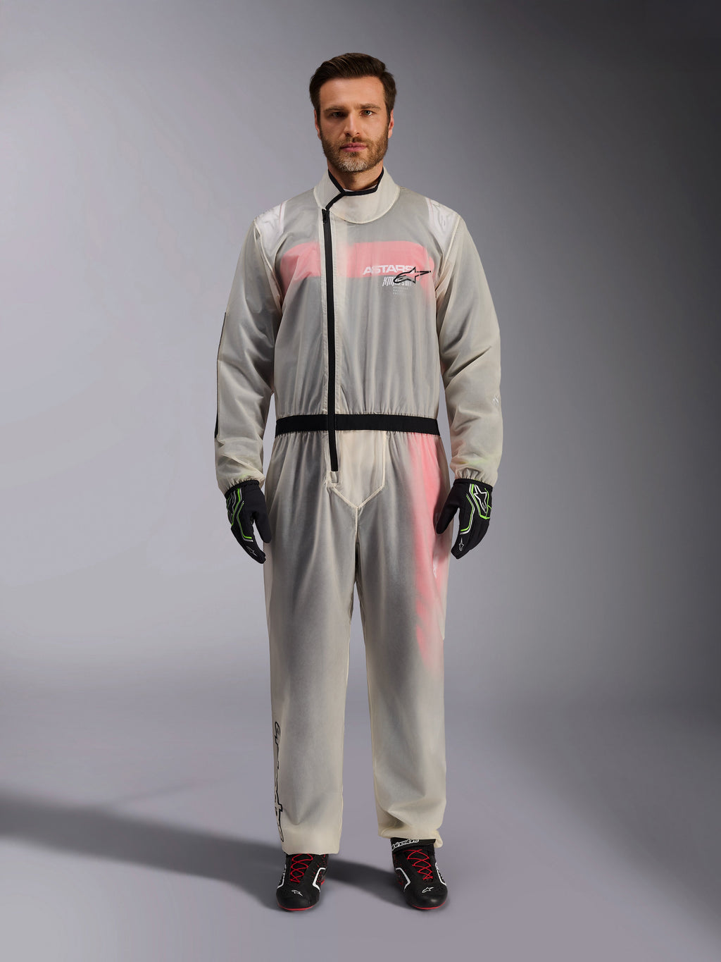 Macacão de Chuva para Kart Alpinestars, Clear, sobre-macacão impermeável transparente vestido por um modelo, com fecho de correr assimétrico preto e logótipo no peito, fato de corrida vermelho e branco visível por baixo, acompanhado por luvas pretas e verde néon e botas de corrida pretas.