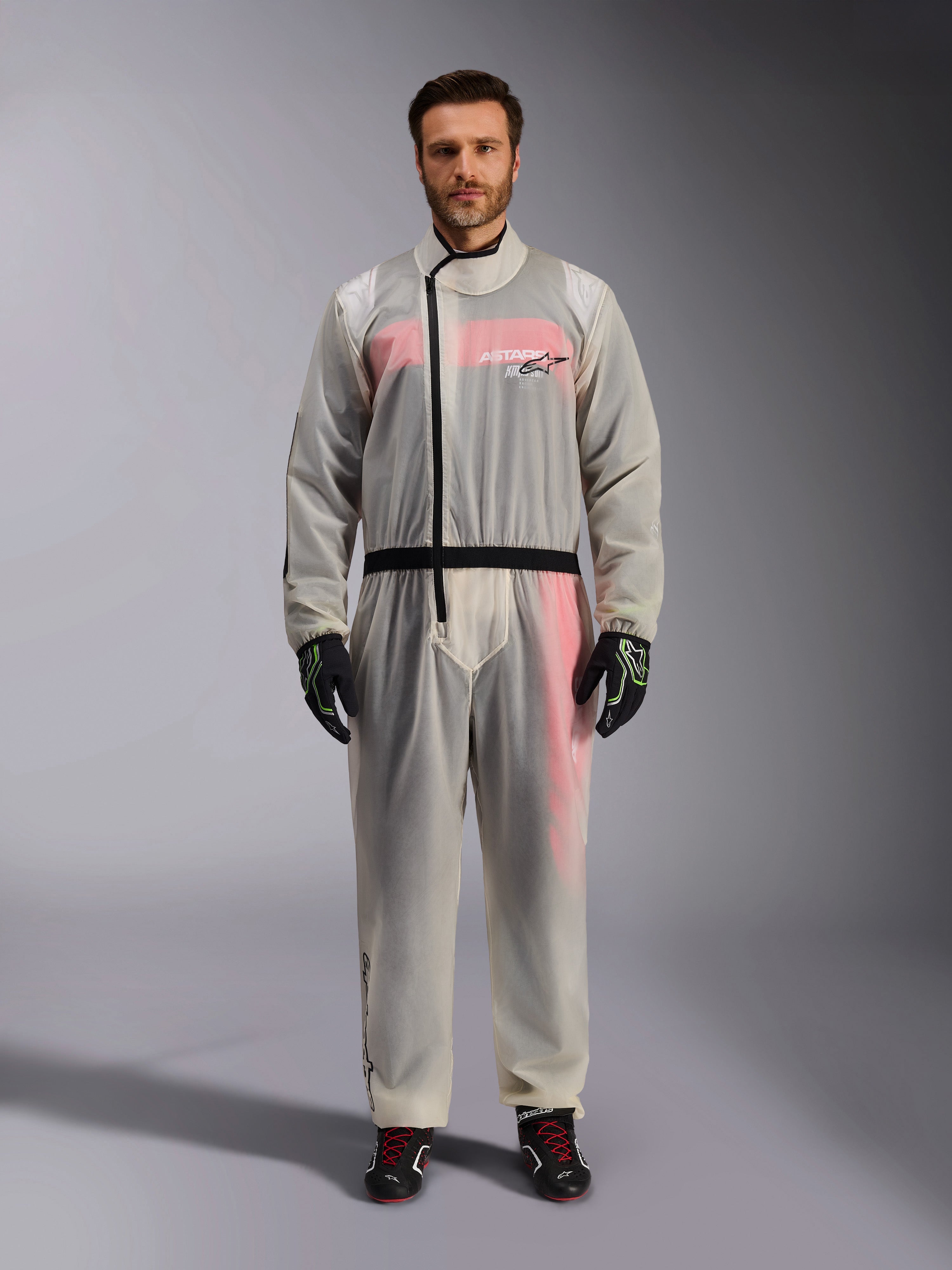 Macacão de Chuva para Kart Alpinestars, Clear, sobre-macacão impermeável transparente vestido por um modelo, com fecho de correr assimétrico preto e logótipo no peito, fato de corrida vermelho e branco visível por baixo, acompanhado por luvas pretas e verde néon e botas de corrida pretas.