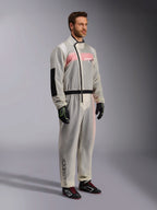 Alpinestars Kart Rain Suit, macacão de chuva para karting transparente e impermeável, material semitransparente que mostra um fato de corrida cor-de-rosa e branco por baixo, com fecho assimétrico preto, reforço no cotovelo e faixa elástica preta na cintura, usado com luvas de karting e sapatos de competição pretos