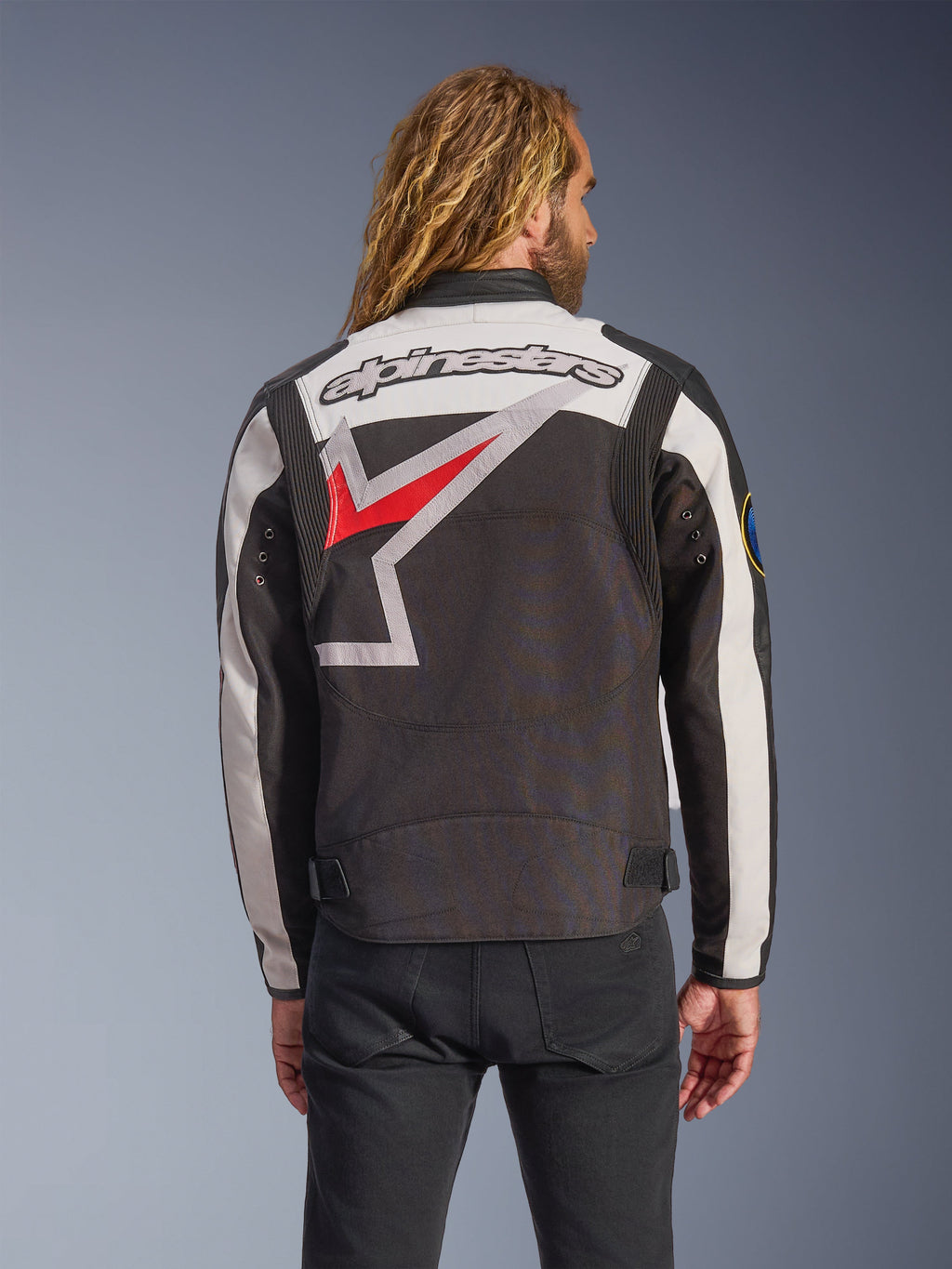Casaco Alpinestars Axton, casaco de motociclismo, preto, off-white e vermelho brilhante, vista traseira com um grande logótipo de estrela envolvente e marca nominativa, design de inspiração vintage com painéis de acordeão nos ombros e ajustadores na cintura