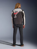 Casaco Alpinestars Axton, casaco de motociclismo, preto, branco sujo e vermelho vivo, vista traseira num modelo, com um logótipo de estrela Alpinestars de grandes dimensões nas costas, painéis das mangas em branco sujo, usado com calças pretas, design inspirado no vestuário de equipa de corrida vintage