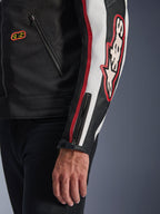 Casaco Alpinestars Axton, grande plano da manga e do tronco, preto com detalhes em branco sujo e vermelho vivo, com logótipo Alpinestars grande bordado no braço, riscas de corrida verticais, punho com fecho de correr e mola de pressão, e construção têxtil resistente