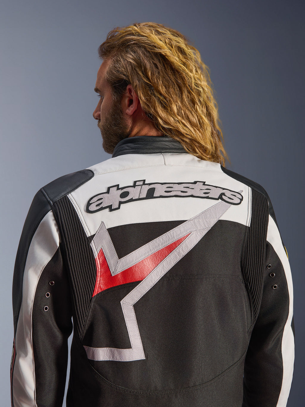Casaco Alpinestars Axton, casaco de motociclismo, preto, off-white e vermelho brilhante, vista traseira com grande logótipo Alpinestars bordado e gráfico estilizado, painéis de acordeão nos ombros para mobilidade, design de inspiração vintage com detalhes de ilhós metálicos