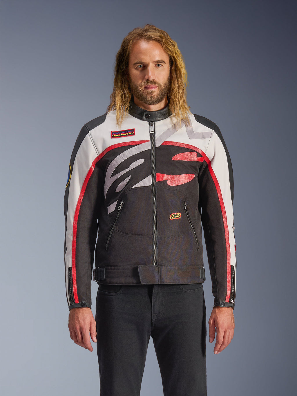 Casaco Alpinestars Axton, casaco de motociclismo, preto, branco e vermelho vivo, com padrões abstratos no peito e logótipo envolvente, mangas com riscas vermelhas, design de inspiração vintage e gola minimalista, usado por modelo com calças de ganga pretas