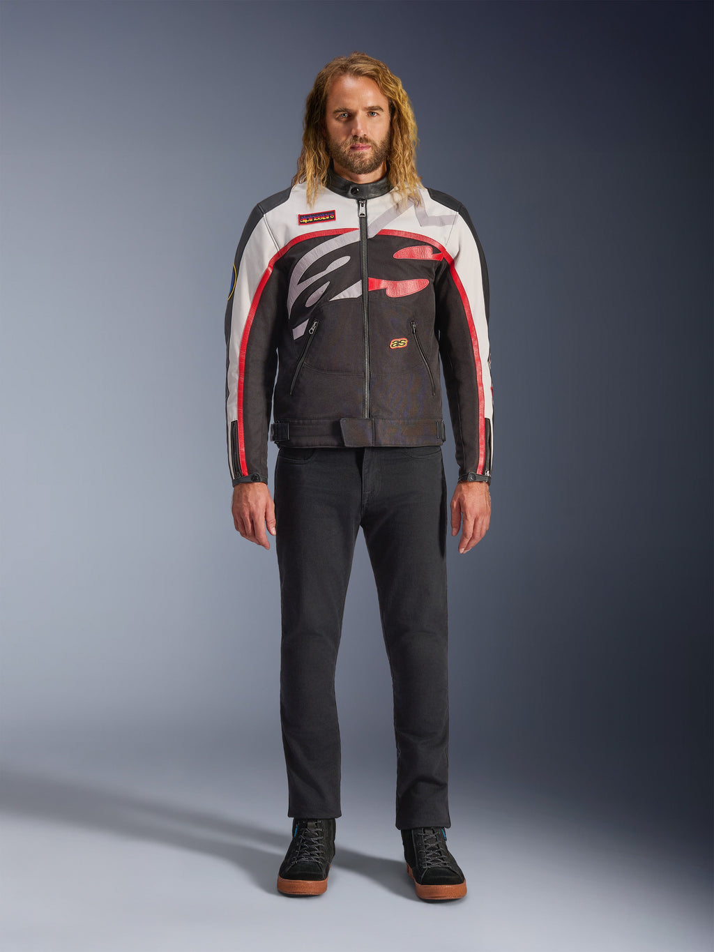 Casaco Alpinestars Axton, casaco de motociclismo, preto, branco sujo e vermelho vivo, usado por um modelo com calças pretas e sapatilhas, com um logótipo envolvente arrojado e design inspirado no estilo de corrida vintage