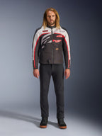 Casaco Alpinestars Axton, casaco de motociclismo, preto, branco sujo e vermelho vivo, usado por um modelo com calças pretas e sapatilhas, com um logótipo envolvente arrojado e design inspirado no estilo de corrida vintage
