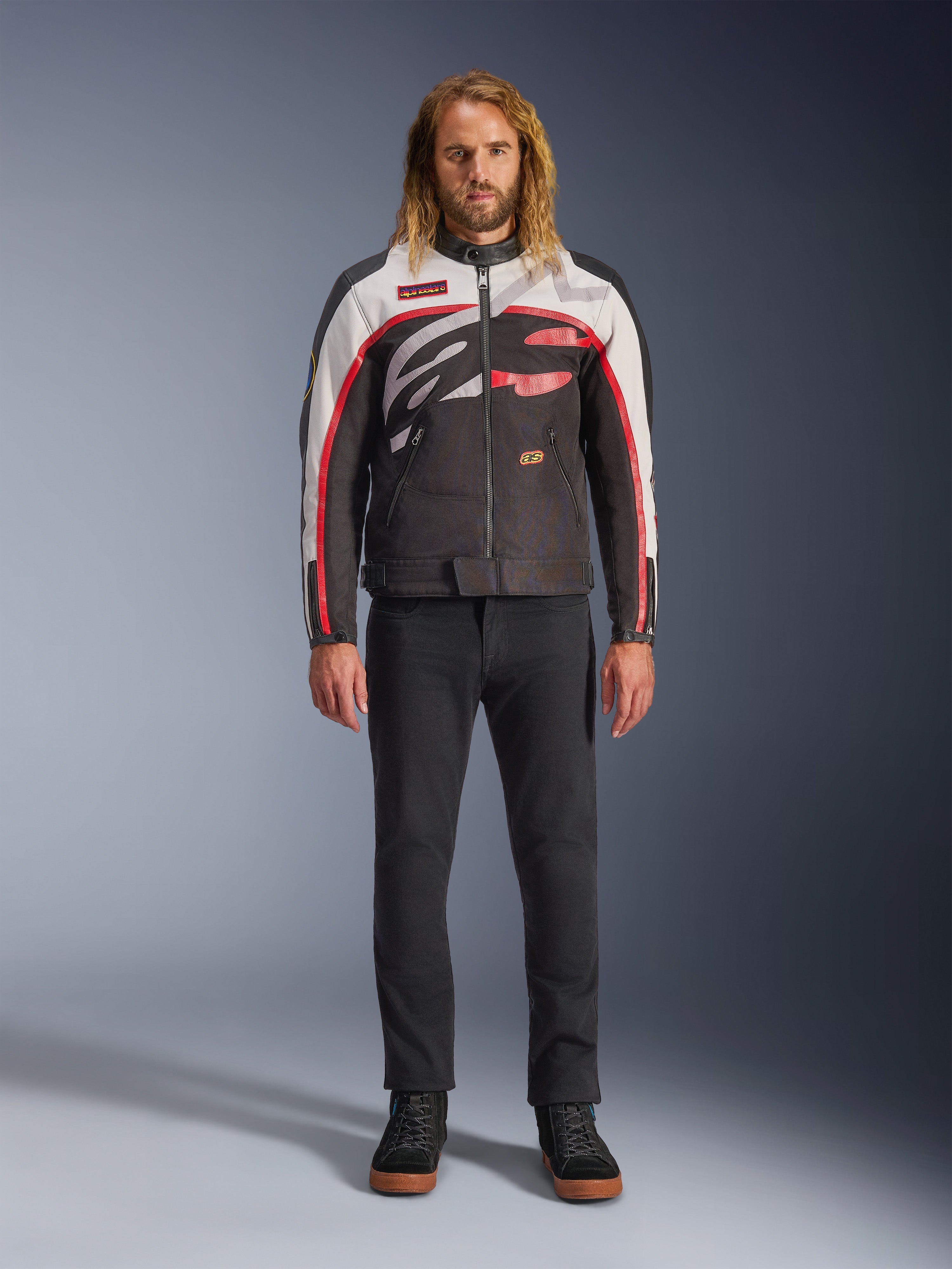 Casaco Alpinestars Axton, casaco de motociclismo, preto, branco sujo e vermelho vivo, usado por um modelo com calças pretas e sapatilhas, com um logótipo envolvente arrojado e design inspirado no estilo de corrida vintage