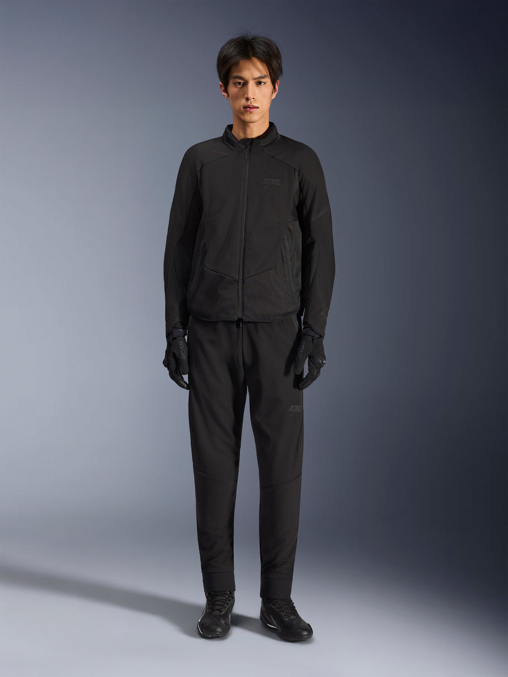 Casaco Alpinestars Aeroshell Airflow, casaco de motociclismo preto, usado por modelo com calças e luvas pretas a condizer, com peito perfurado a laser e painéis de malha laterais, corte desportivo para desempenho em clima quente