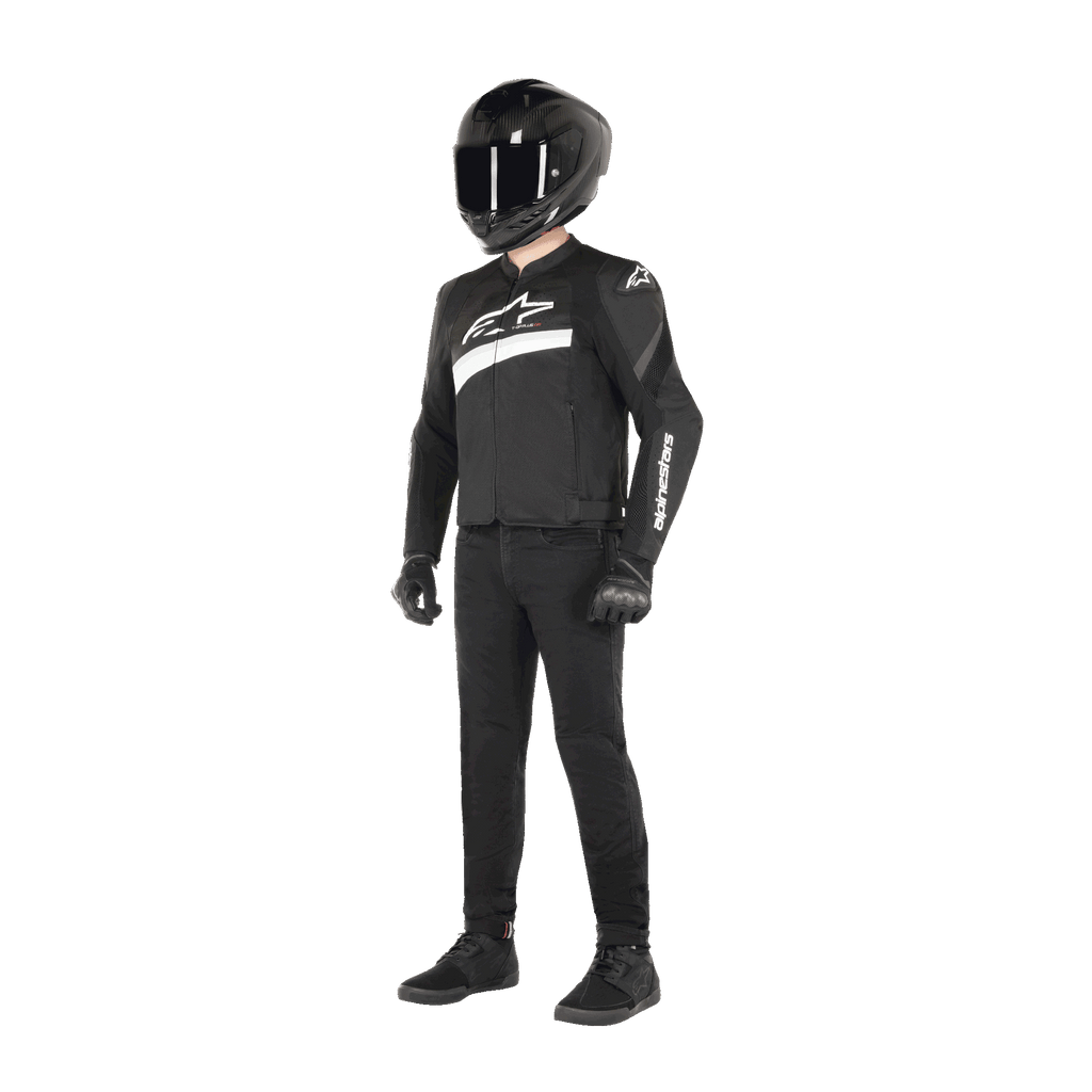 Piloto a usar Casaco Alpinestars T-GP Plus R V4 Airflow em preto e branco, casaco de motociclismo em tecido com painéis de malha e marca Alpinestars em branco, acompanhado por capacete preto, luvas de pilotagem pretas, calças pretas e sapatos pretos