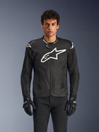 Alpinestars T-GP Air Jacket, casaco de motociclismo têxtil preto com um grande logótipo de estrela branco no peito, apresenta painéis de ventilação perfurados e malha 3D, deslizadores externos nos ombros, usado com luvas pretas e brancas, design desportivo elegante para condução em estrada com tempo quente